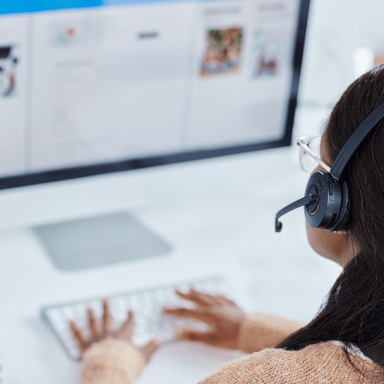 Person mit Headset arbeitet am Computer, Bildschirm zeigt Inhalte, Hände auf der Tastatur.
