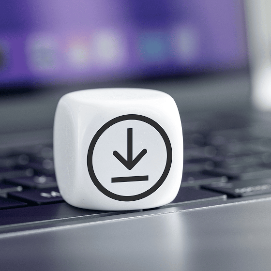 Weißer Würfel mit einem Download-Symbol auf einer Tastatur mit verschwommenem Hintergrund.