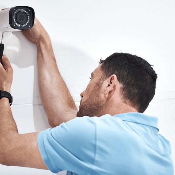 Ein Mann installiert eine Überwachungskamera an einer weißen Wand.